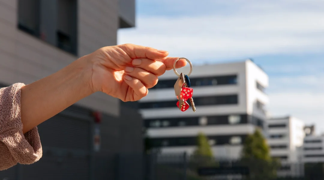 A person holds a key in front of a building, symbolizing access or entry to the property.