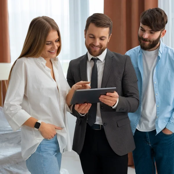 Guide du courtier immobilier à Montréal pour investir 2 Trois personnes se tenant devant une tablette numérique, discutant de son contenu.