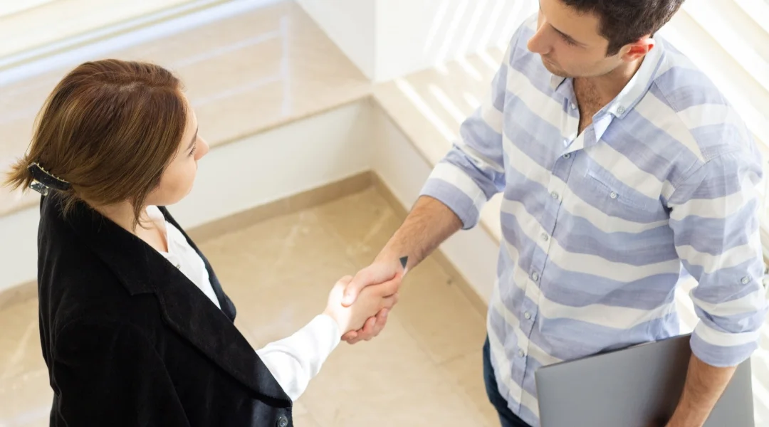 A man and woman shaking hands in a modern office setting, symbolizing a professional agreement or partnership.
