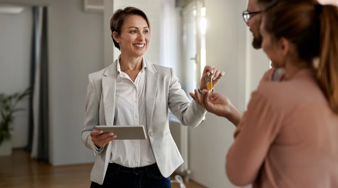 A woman hands a key to a man and a woman, symbolizing the transfer of ownership or responsibility.