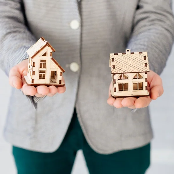Comment choisir le bon type de propriété à Montréal 3 Un homme tient deux petites maisons en bois dans ses mains, illustrant un projet de construction ou d'artisanat.